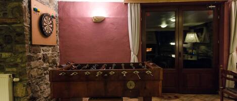 A foosball table in a room with a dartboard on the wall, a stone wall, and a door leading to another room.