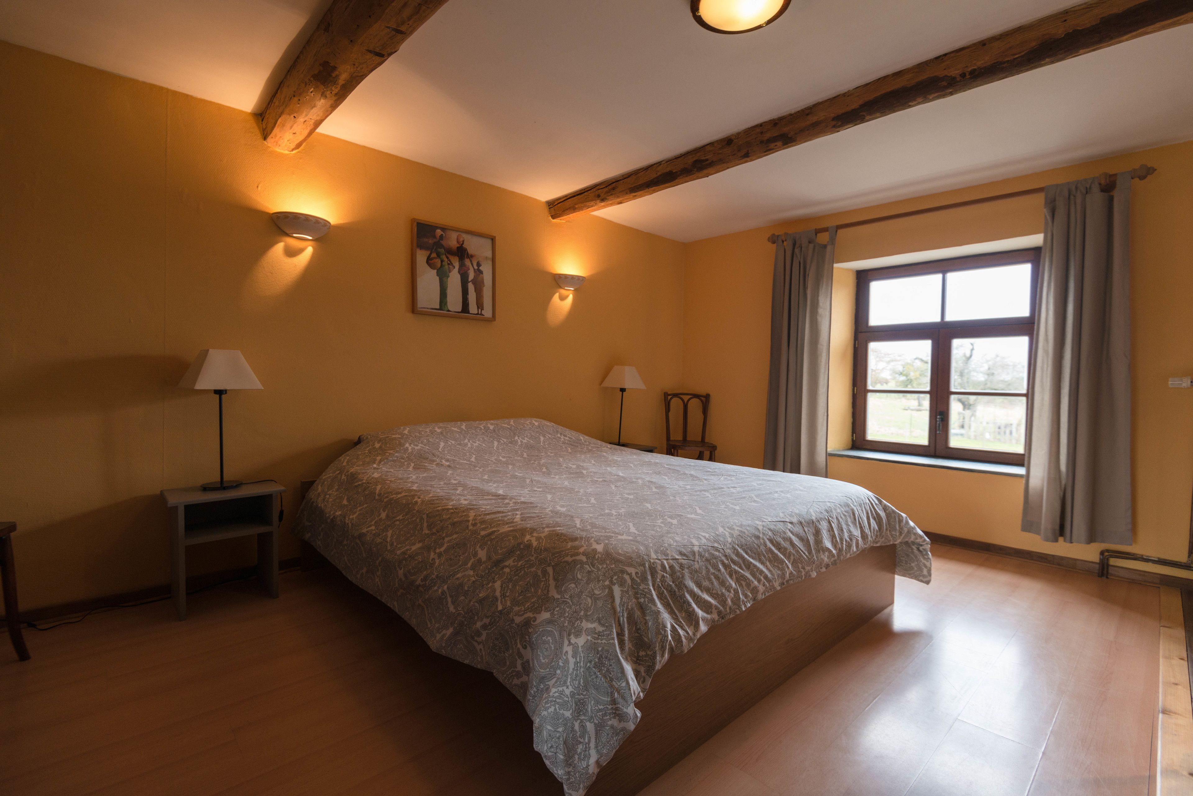 Ein Schlafzimmer mit einem großen Bett, zwei Nachttischlampen, einem Bild an der Wand und einem Fenster mit Vorhängen.