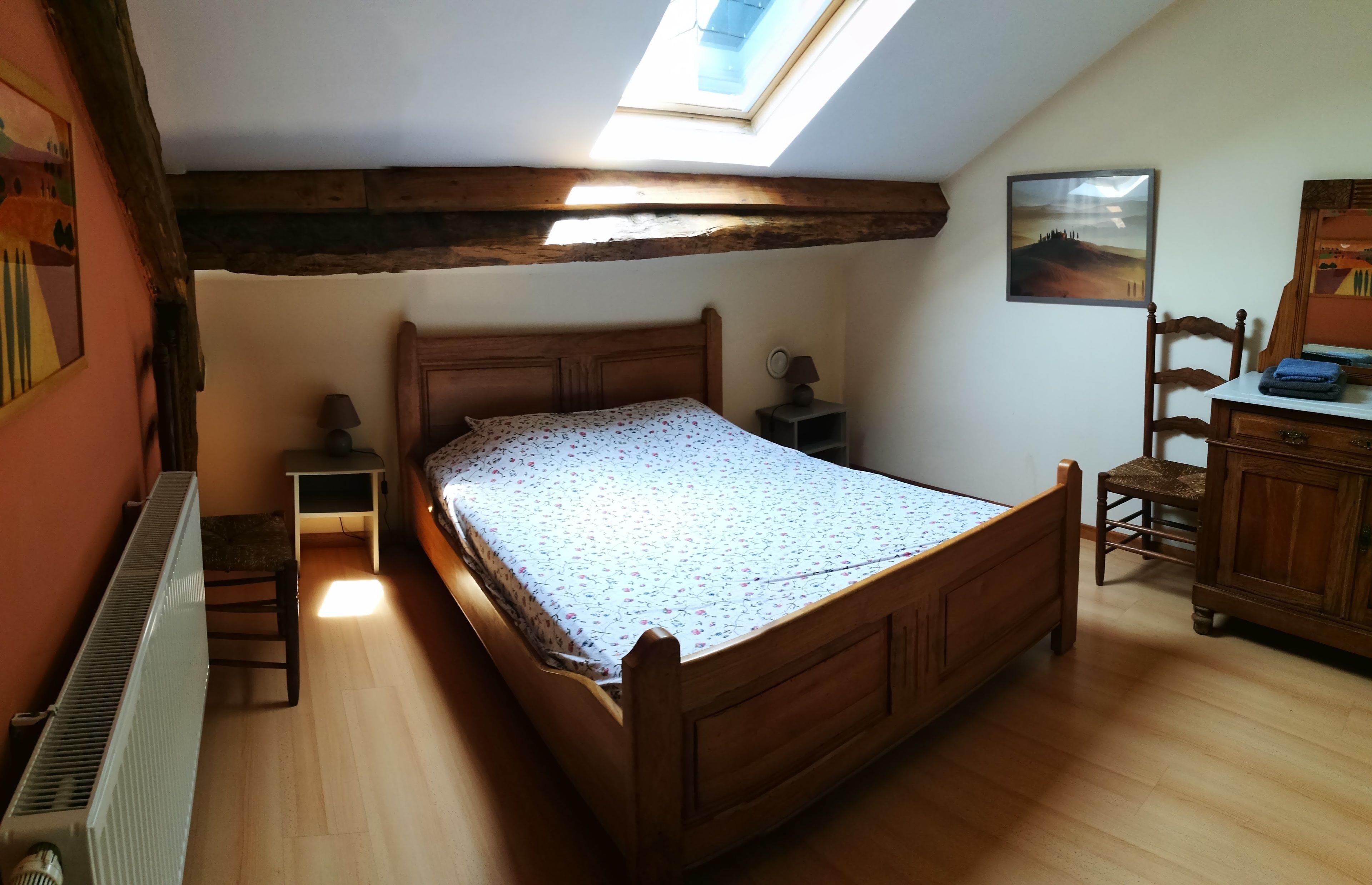 A bedroom with a wooden bed, a skylight, a radiator, and a small bedside table with a lamp.