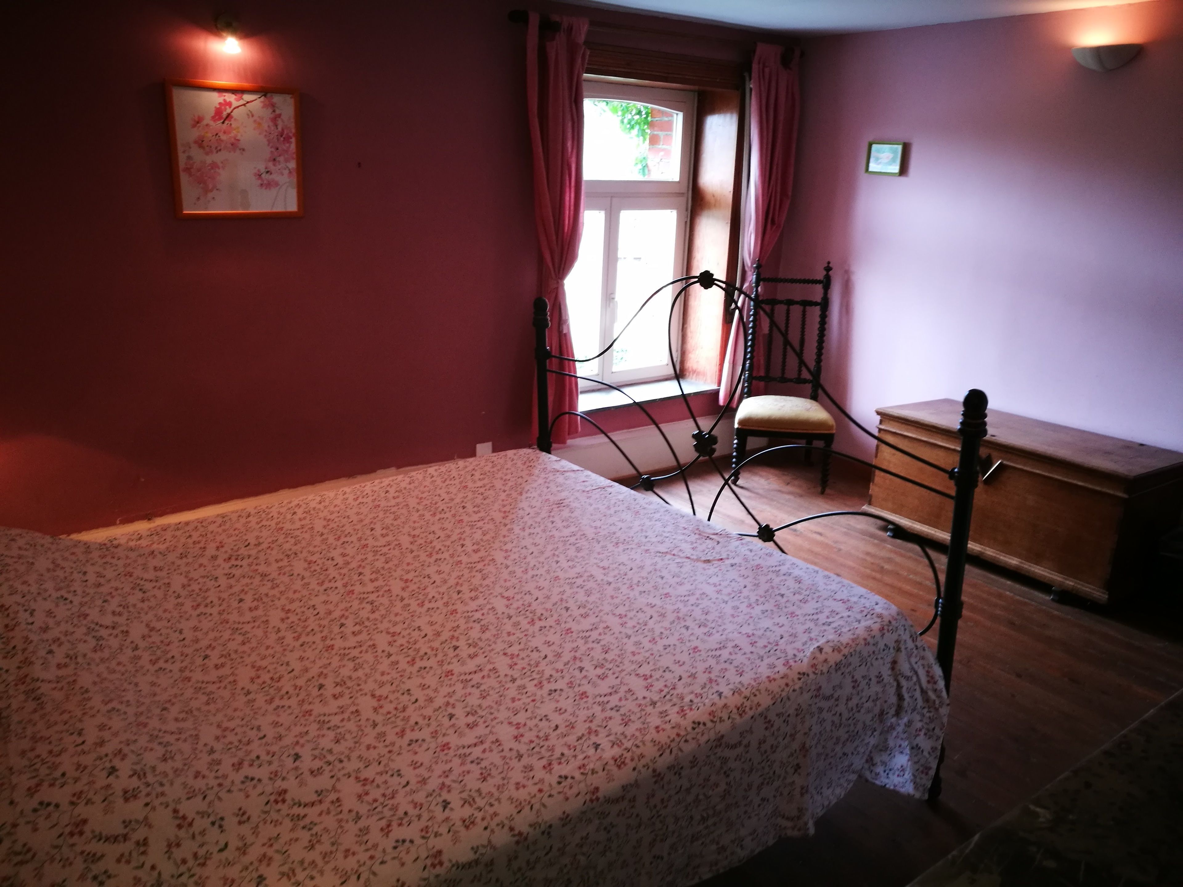 A bedroom with a bed, a chair, a wooden dresser, and a window with curtains.