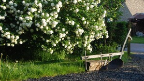 A garden with a wooden bench and a stone building in the background. - B&B Les Trois Voisins (Gedinne)