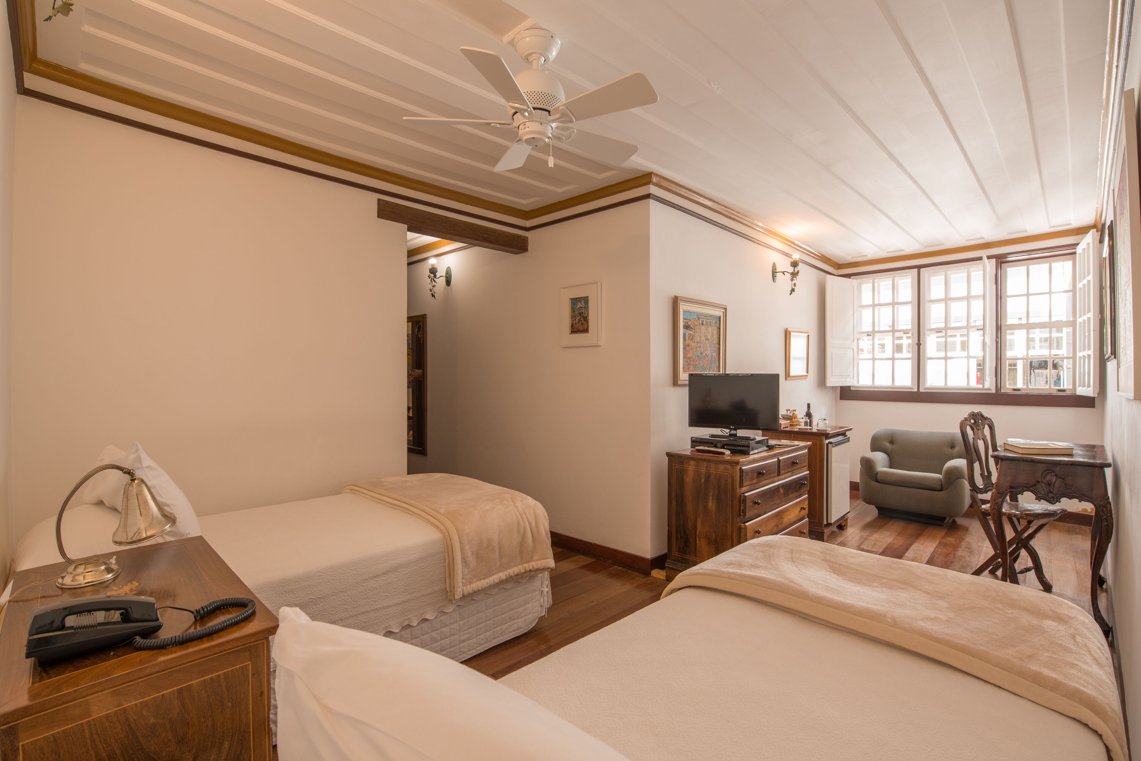 A hotel room with two beds, a desk with a television, a chair, and a wooden dresser.