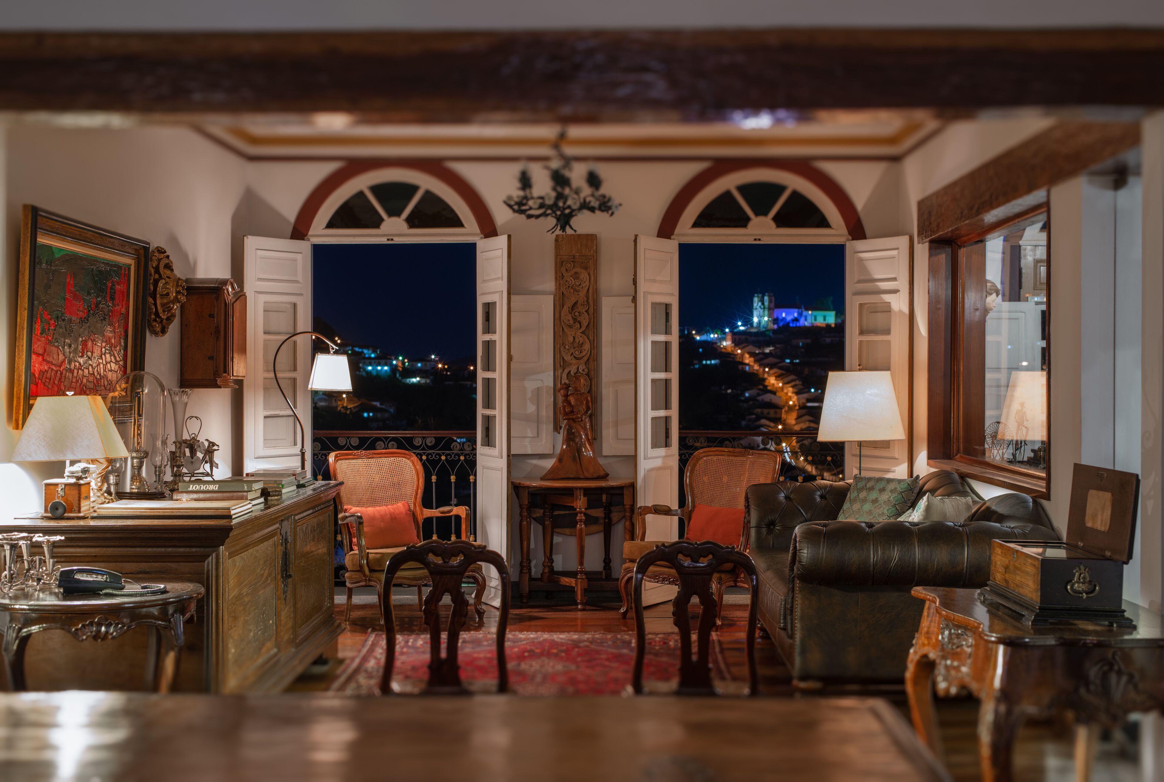 Habitación con vista a un paisaje urbano nocturno, que incluye un sofá, sillas, una mesa y una lámpara.