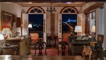 A room with a view of a cityscape at night, featuring a sofa, chairs, a table, and a lamp.