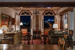 A room with a view of a cityscape at night, featuring a sofa, chairs, a table, and a lamp. - Pousada do Mondego (Ouro Preto)