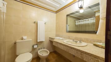 A bathroom with a toilet, bidet, sink, and mirror.