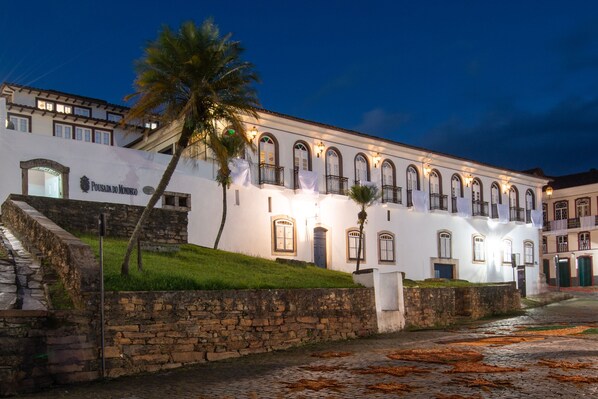 A historic building with a stone facade, arched windows, and a palm tree in front. - Pousada do Mondego (Ouro Preto)