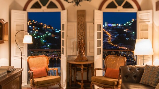 A cozy room with two armchairs, a sofa, and a table. Large windows offer a view of a cityscape at night. - Pousada do Mondego (Ouro Preto)