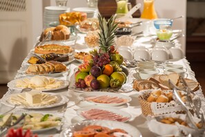 A buffet table with various breakfast items including fruits, pastries, and meats. - Pousada do Mondego (Ouro Preto)