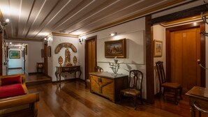 A spacious hallway with wooden flooring, a red upholstered chair, a wooden cabinet, and a painting on the wall. - Pousada do Mondego (Ouro Preto)