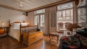 A bedroom with a wooden bed, a nightstand, a dresser, and a window with a view of a balcony. - Pousada do Mondego (Ouro Preto)