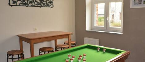Een pooltafel met krukken, een houten tafel en een raam met uitzicht.