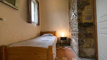 Un dormitorio pequeño y acogedor con una cama de madera, una mesita de noche con lámpara y una pared de piedra.