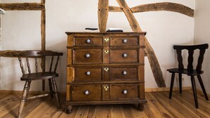 A wooden dresser with multiple drawers and decorative knobs, positioned against a white wall with exposed wooden beams. - Gîte Les Trois Voisins (Gedinne)