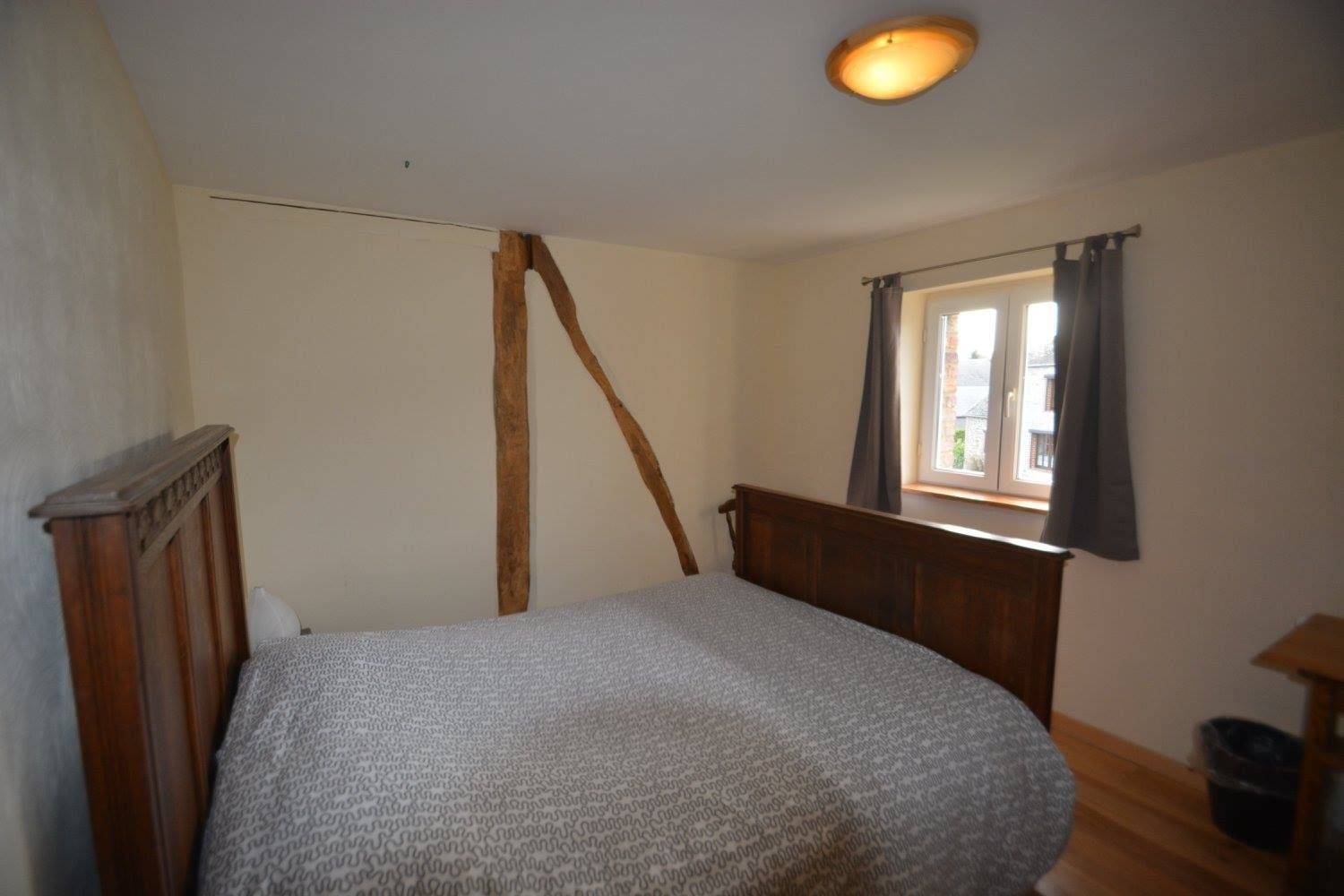 A bedroom with a single bed, a window with curtains, a wooden headboard, and a ceiling light.