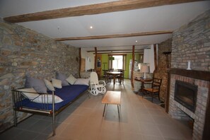 Una habitación rústica con pared de piedra, techo de madera, sofá, mesa de comedor y chimenea.