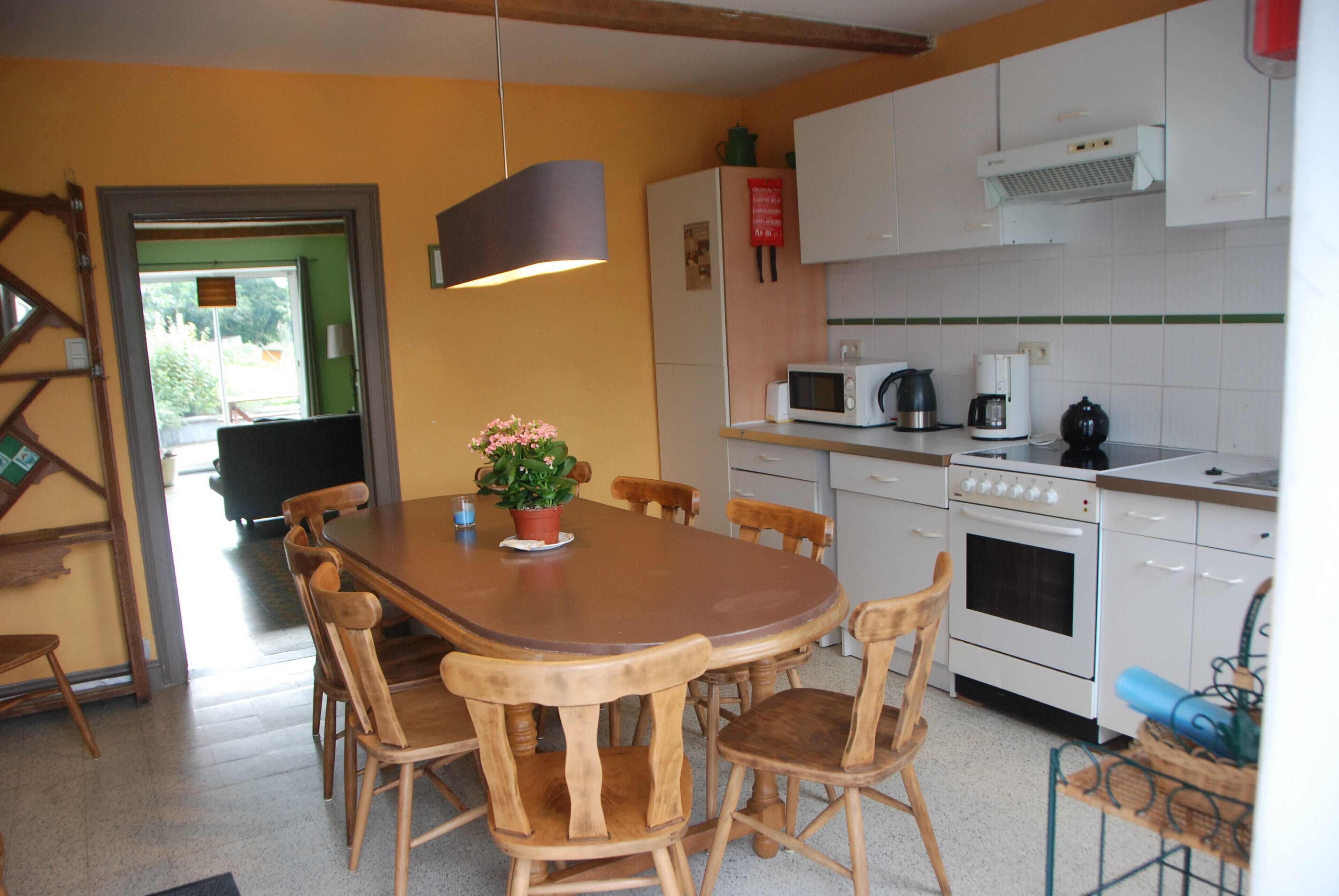 Una cocina con sillas de madera, una mesa, un microondas, una cafetera y un horno.
