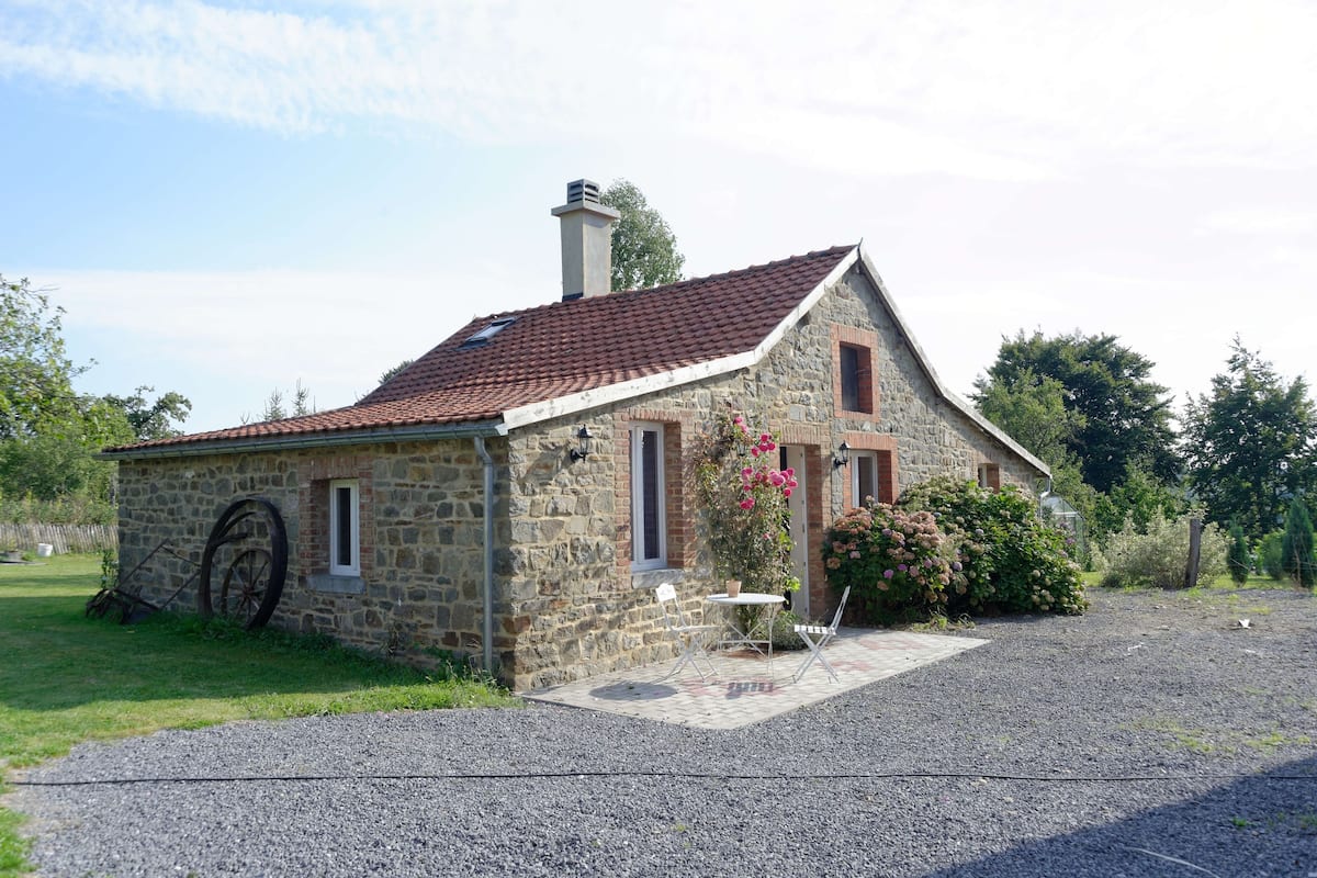 Una casa de piedra con techo de tejas rojas, una chimenea y un camino de entrada de grava.
