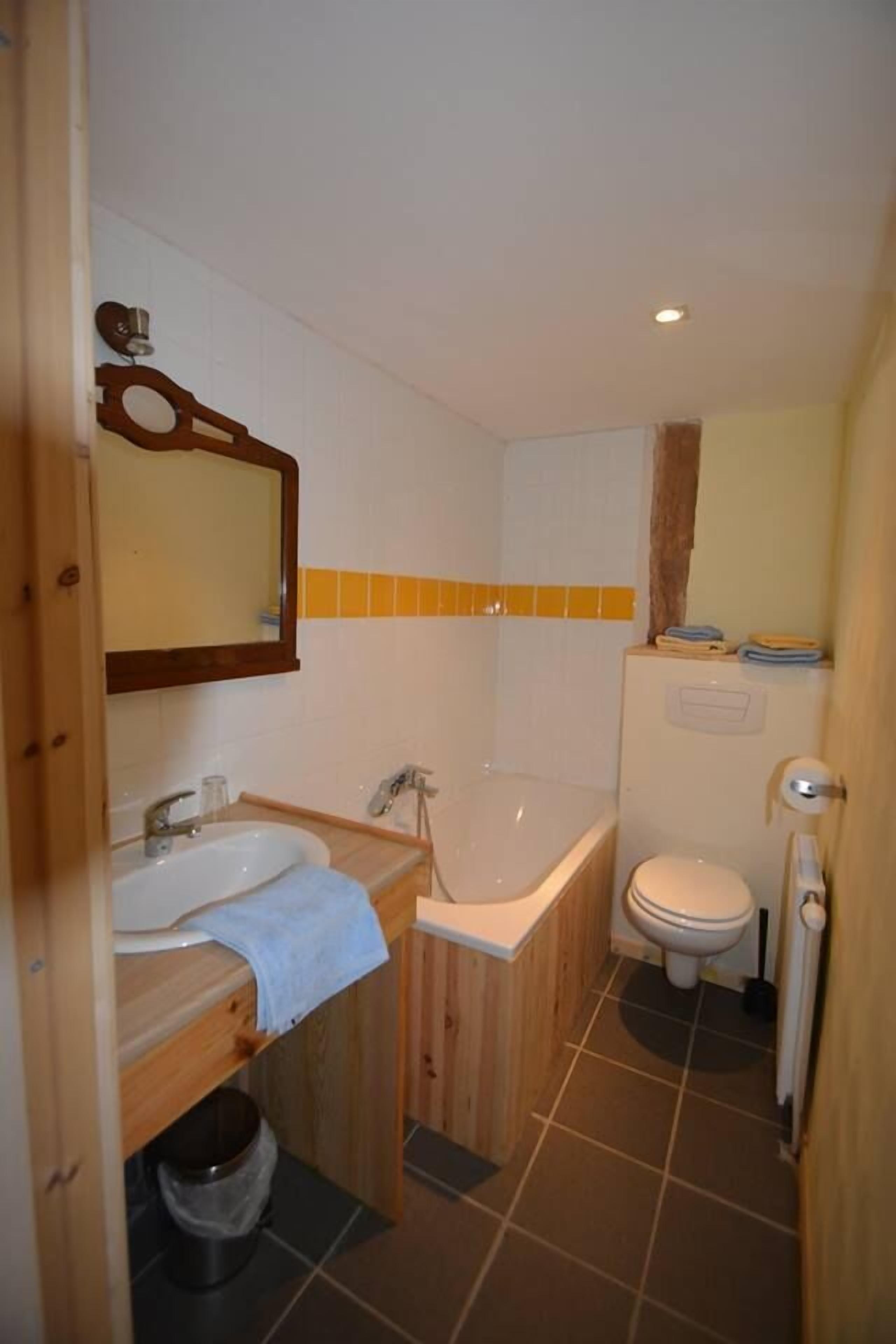 A compact bathroom with a wooden vanity, a sink, a bathtub, and a toilet.