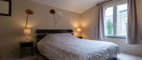 Un dormitorio con una cama grande, dos lámparas de noche, una mesita de noche, una alfombra estampada y un ventanal con cortinas.