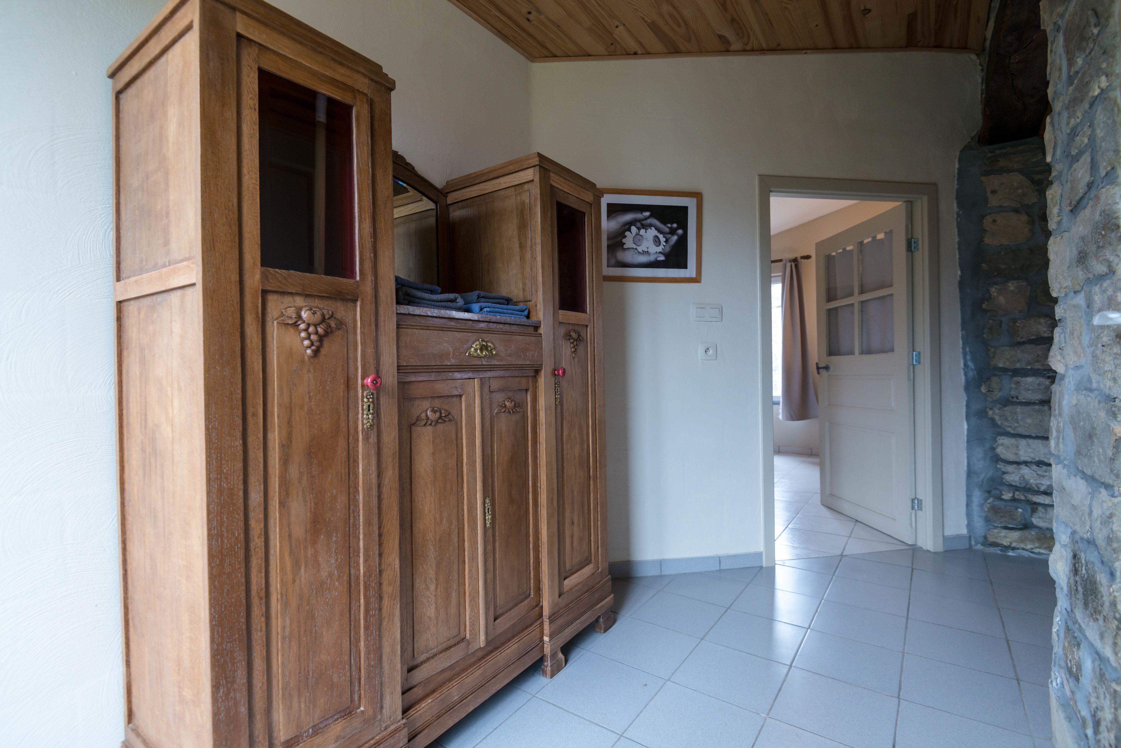 A wooden wardrobe with a mirror, a framed picture on the wall, and a stone wall.