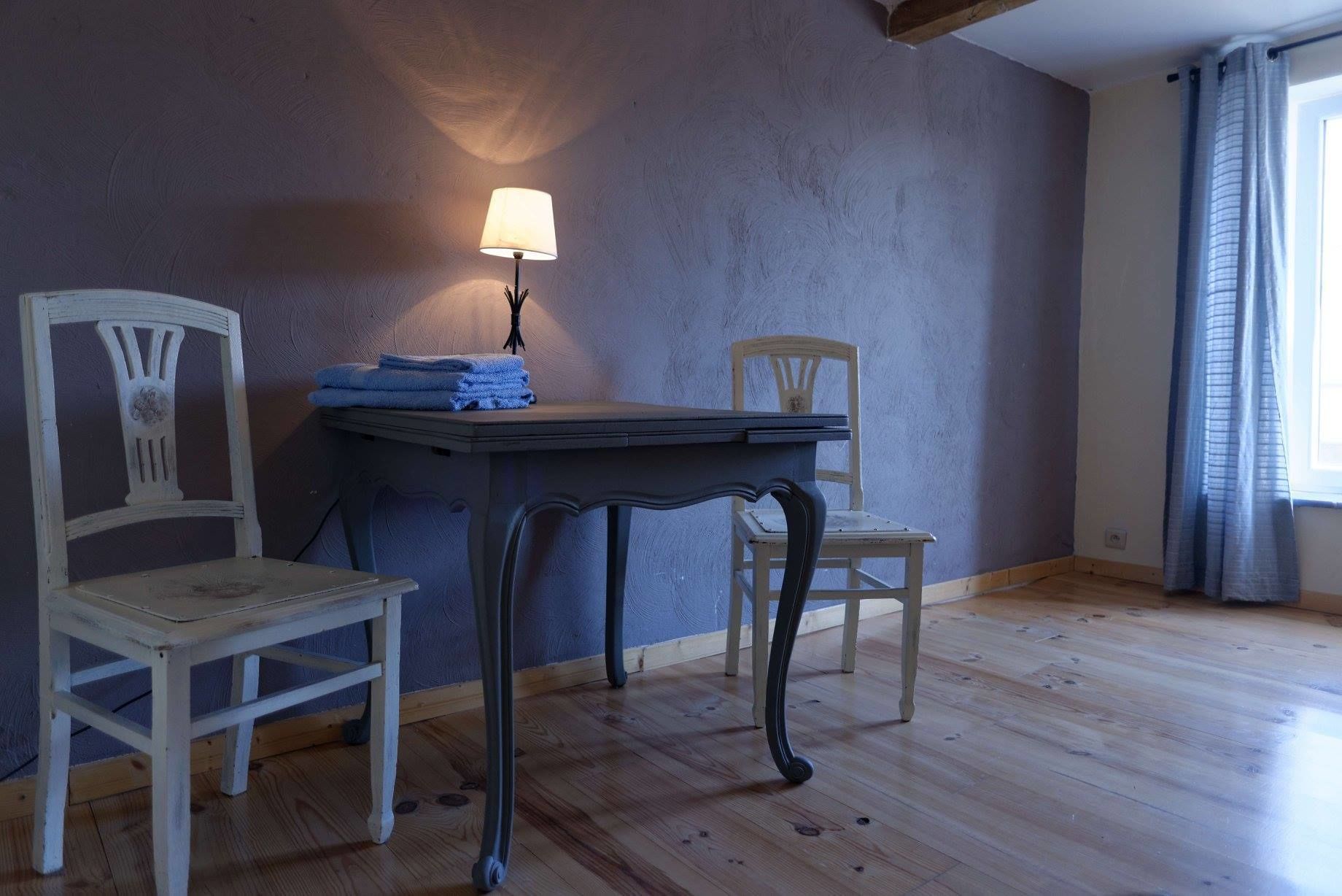 A room with a table, two chairs, a lamp, and a window with curtains.