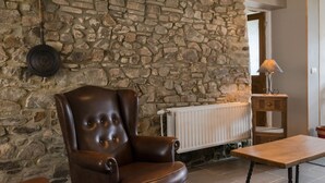 A stone wall, a brown leather armchair, a wooden table, and a radiator. - Gîte Les Trois Voisins (Gedinne)