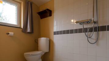A bathroom with a toilet, a shower, and a window with a curtain.