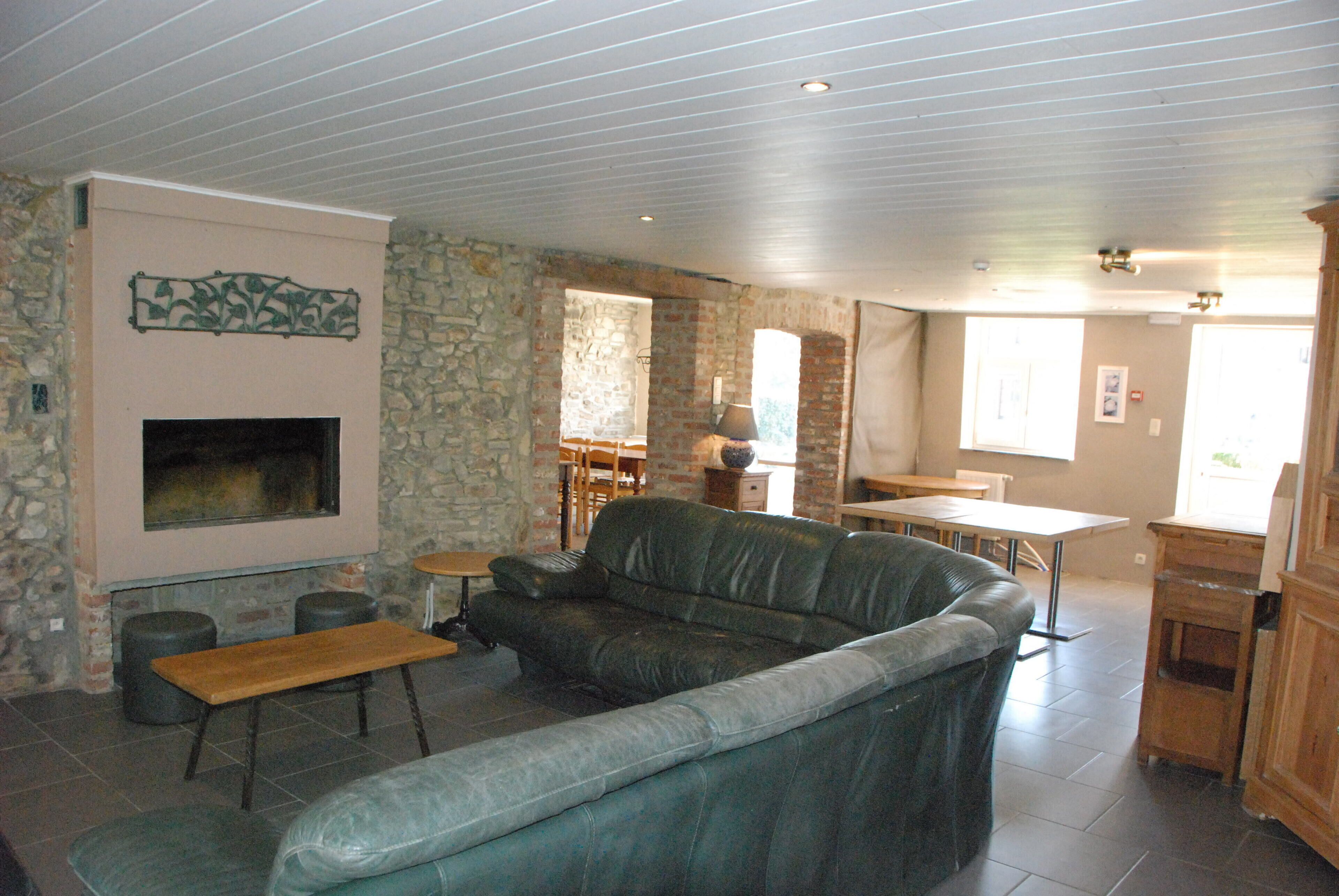 A living room with a stone wall, a fireplace, a leather sofa, a wooden bench, and a dining area with a table and chairs.