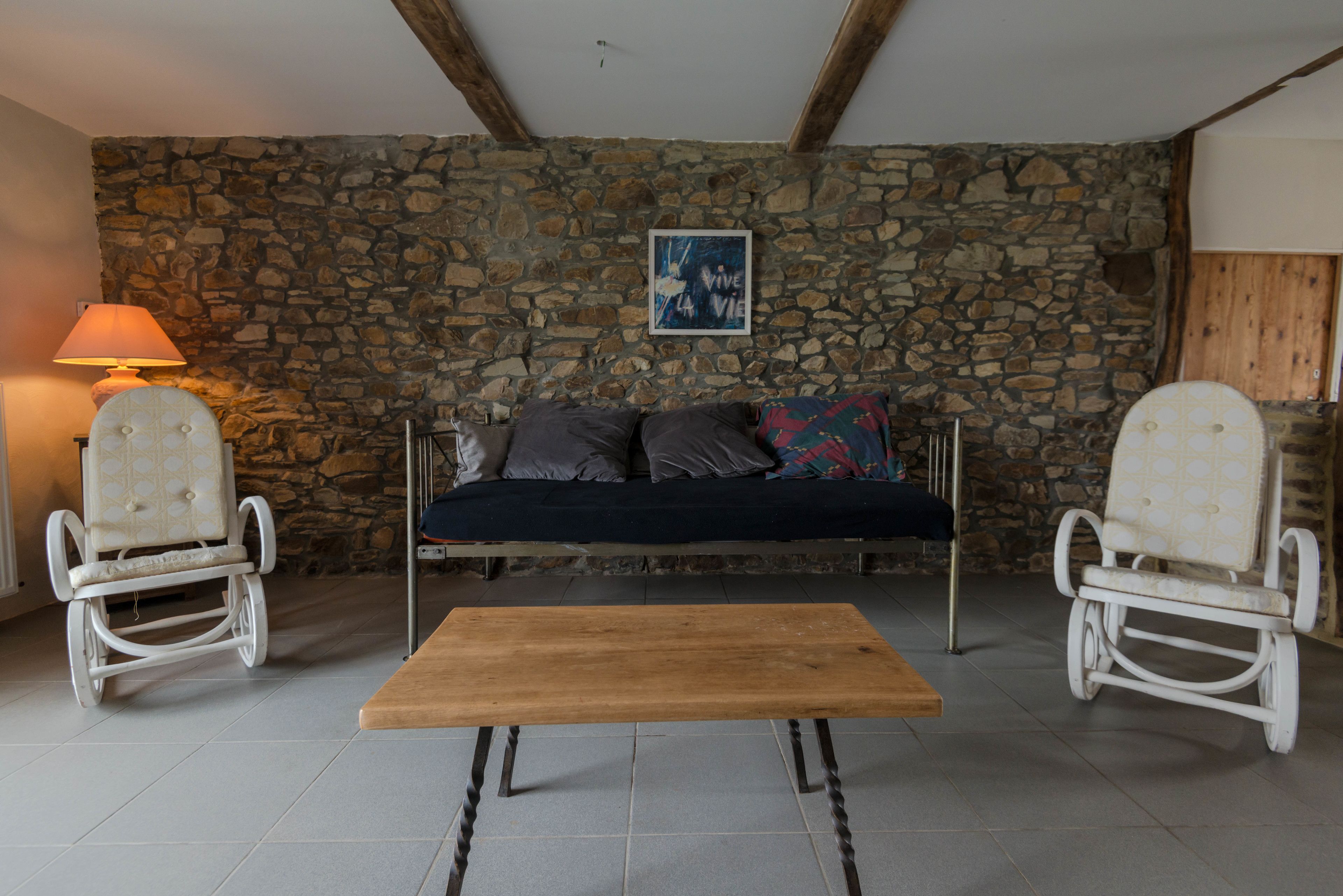A stone-walled room with a sofa, two rocking chairs, and a wooden table.