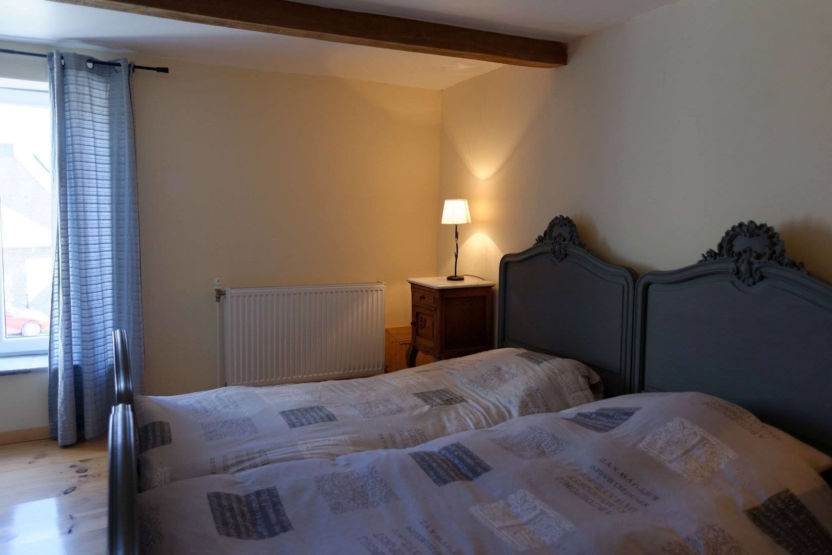 Un dormitorio con dos camas, un radiador, una mesita de noche, una lámpara y una ventana con cortinas.