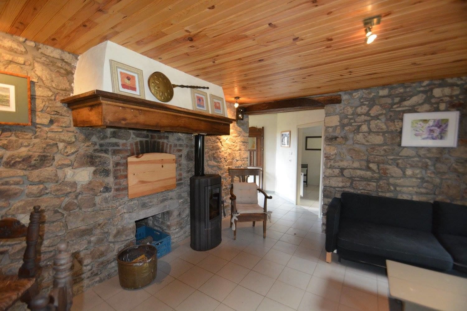 A rustic interior with a stone fireplace, wooden beams, and a black sofa.