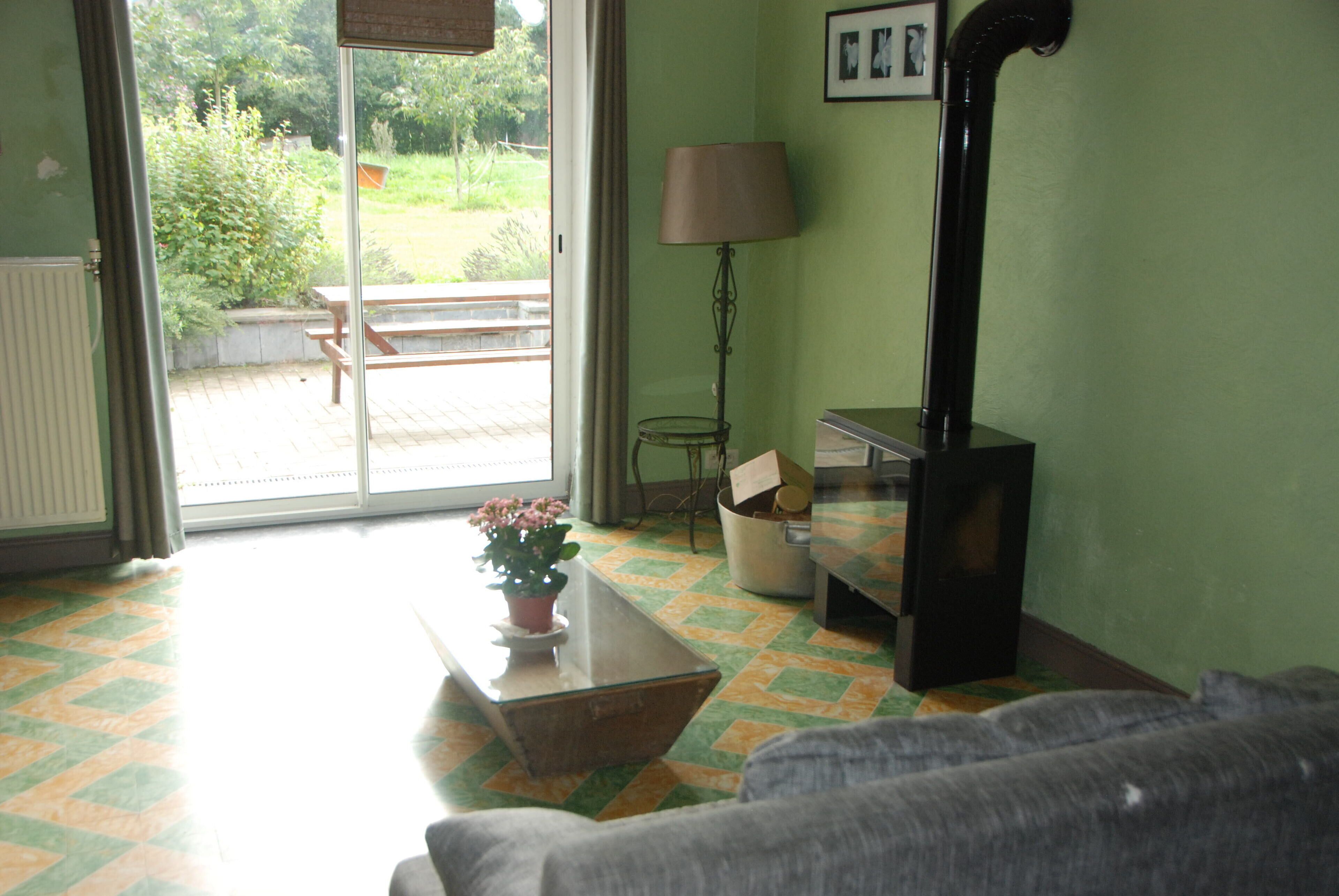 A room with a sofa, a table with a potted plant, a lamp, and a bench outside a sliding glass door.