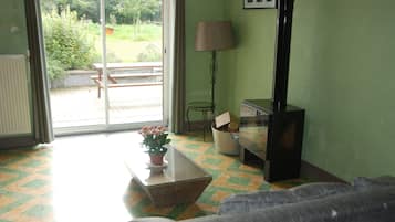A room with a sofa, a table with a potted plant, a lamp, and a bench outside a sliding glass door.