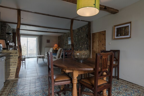 Un espace repas avec une table et des chaises en bois, un mur en pierre et une grande fenêtre.