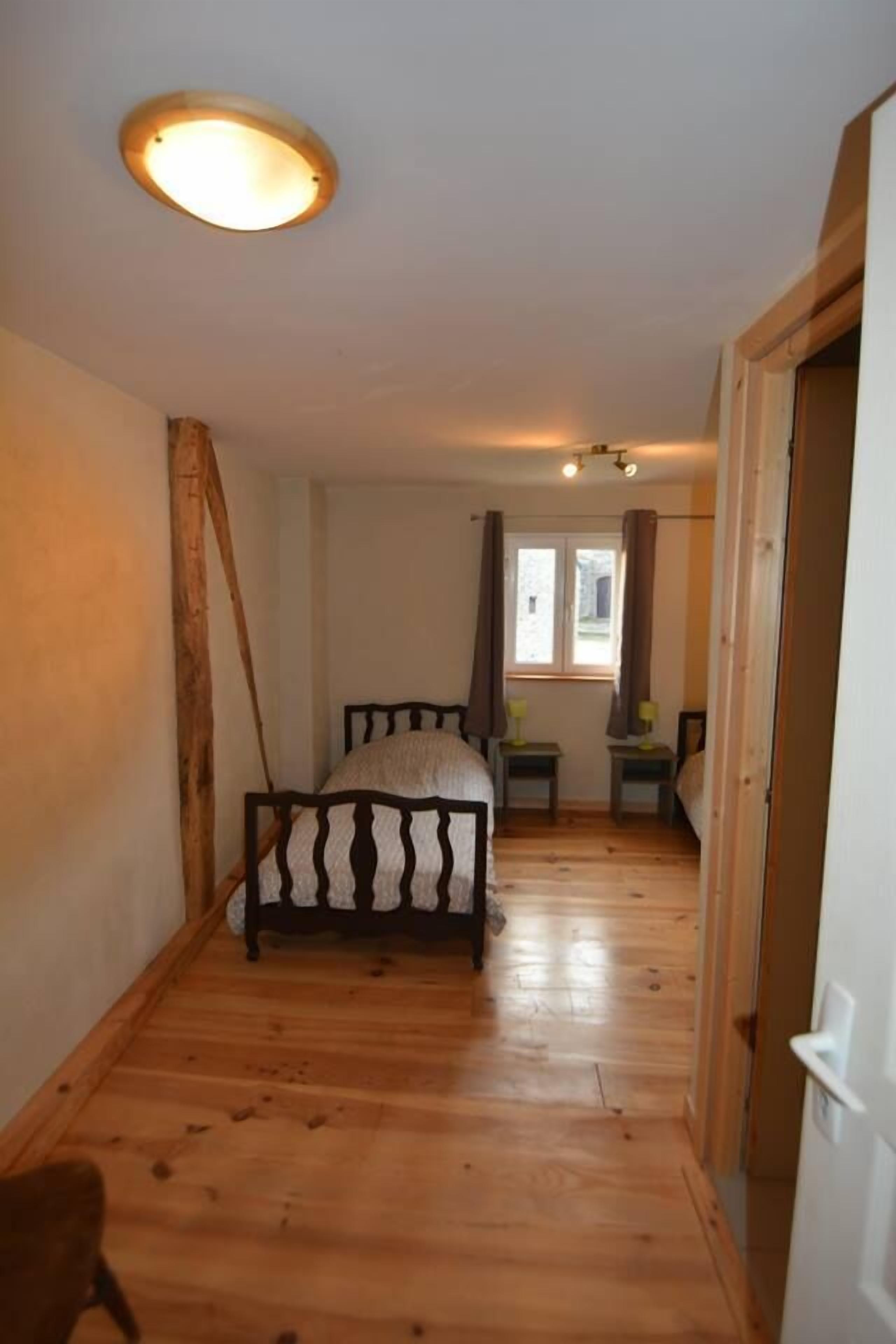 Een slaapkamer met een houten vloer, een bed met hoofdeinde, een raam met gordijnen en een deur.