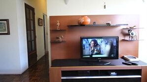 A living room with a television on a wooden entertainment unit, a door, and a hallway. - GoHouse Visconde 802 (Rio de Janeiro)