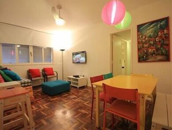A room with a wooden herringbone floor, a yellow table, red chairs, a teal ottoman, and a painting on the wall.
