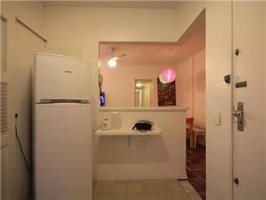 A compact kitchen with a white refrigerator, a small countertop with a coffee maker, and a ceiling fan.