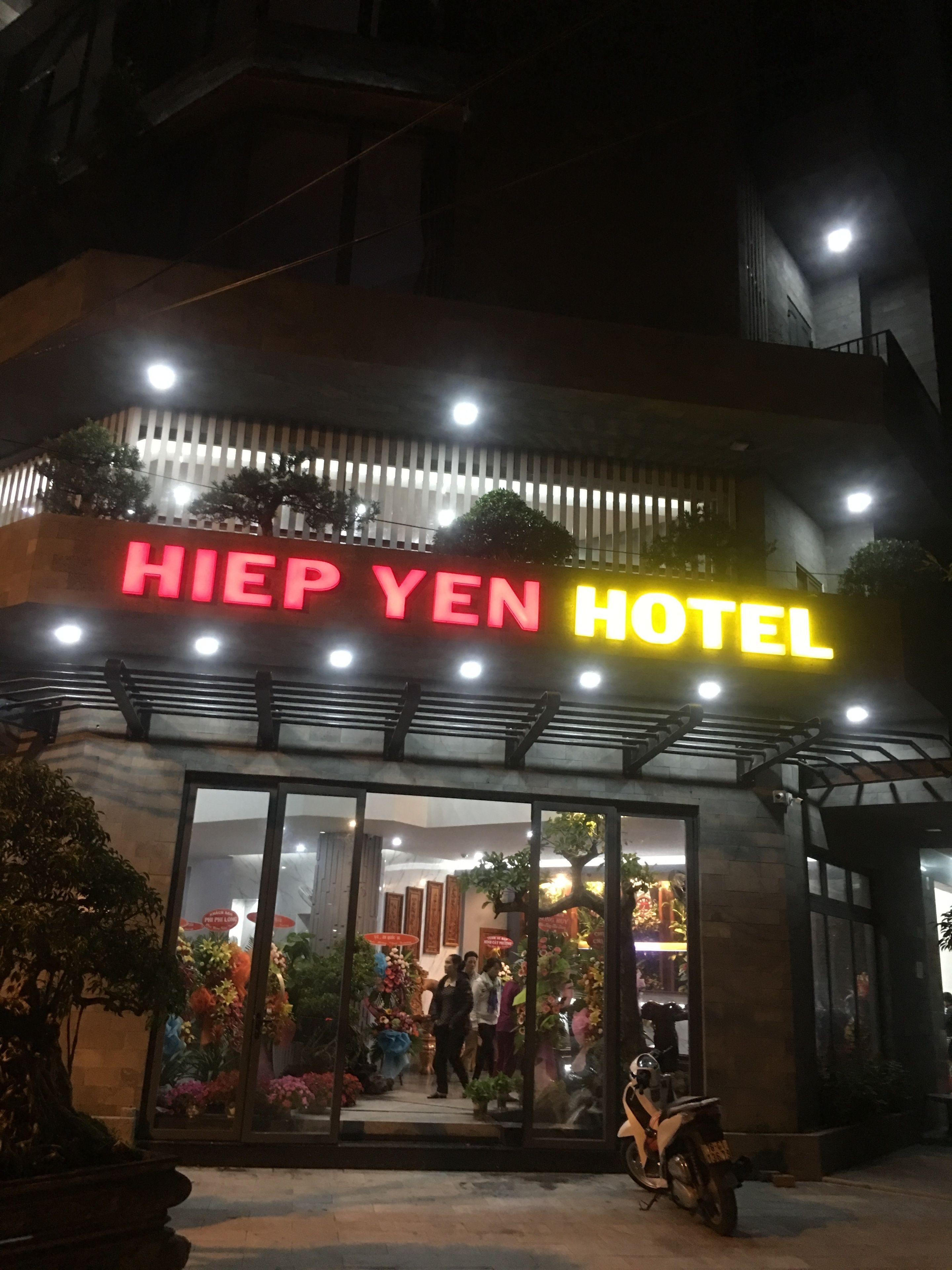 Esterno dell'Hotel Hiep Yen con insegna illuminata, ingresso in vetro e uno scooter parcheggiato davanti.