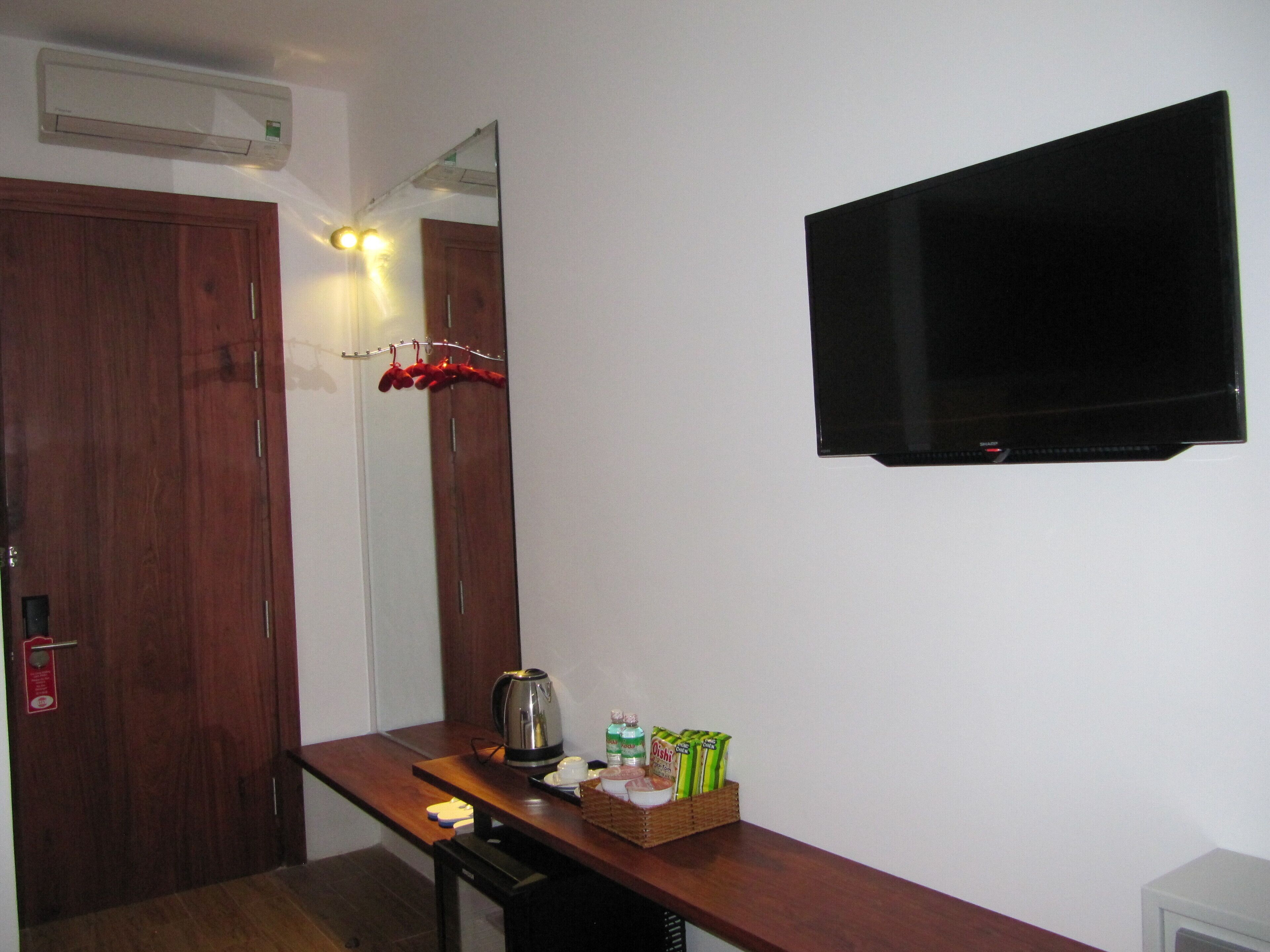 Habitación de hotel con un escritorio de madera, una tetera, una cesta de aperitivos, un espejo y un televisor de pantalla plana montado en la pared.