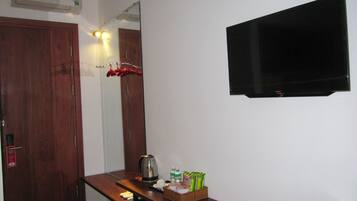 Habitación de hotel con un escritorio de madera, una tetera, una cesta de aperitivos, un espejo y un televisor de pantalla plana montado en la pared.