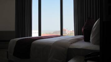 A hotel room with a large bed, a view of the cityscape through floor-to-ceiling windows, and a remote control on the bedside table.