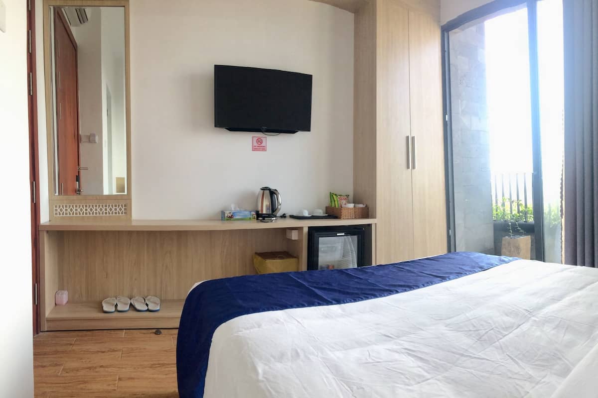 A hotel room with a bed, a television, a small kitchenette, a mirror, and a window with curtains.