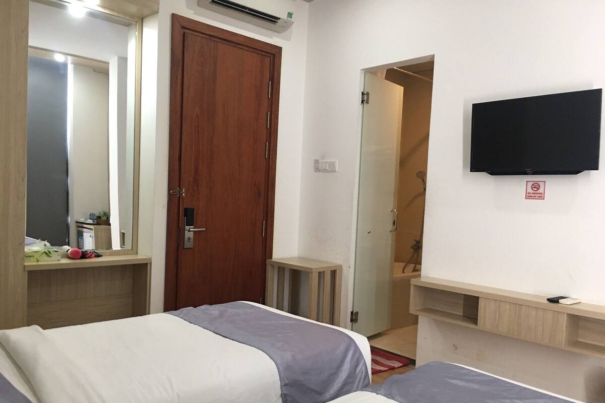 A hotel room with two beds, a wooden door, a mirror, a TV, and a shower area.