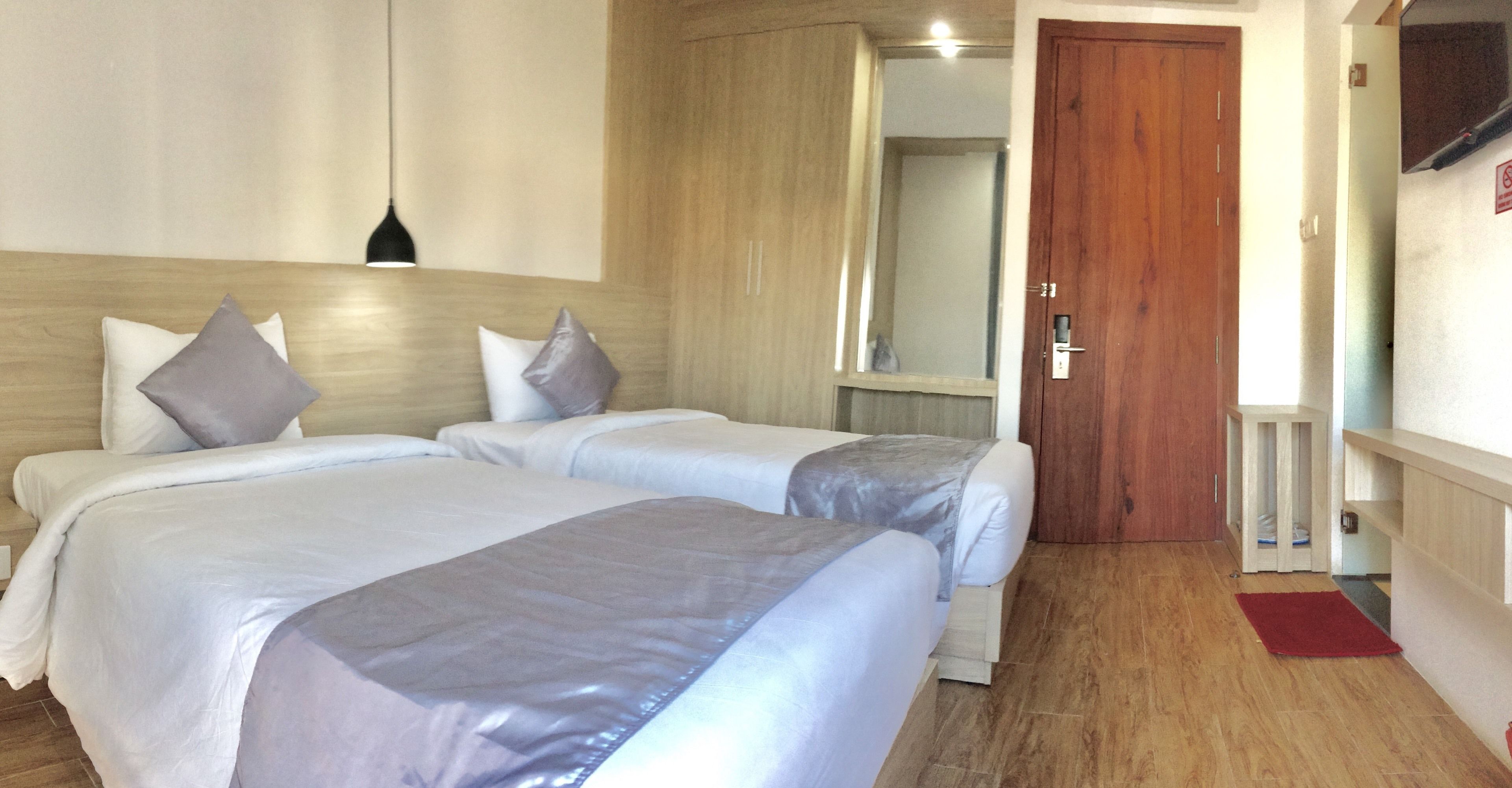 Een hotelkamer met twee bedden, een houten hoofdeinde, een spiegel, een houten deur en een rood vloerkleed.