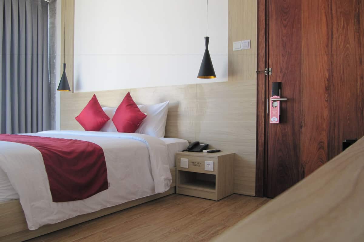 A hotel room with a bed, a nightstand, a wooden door, and a wall-mounted light fixture.