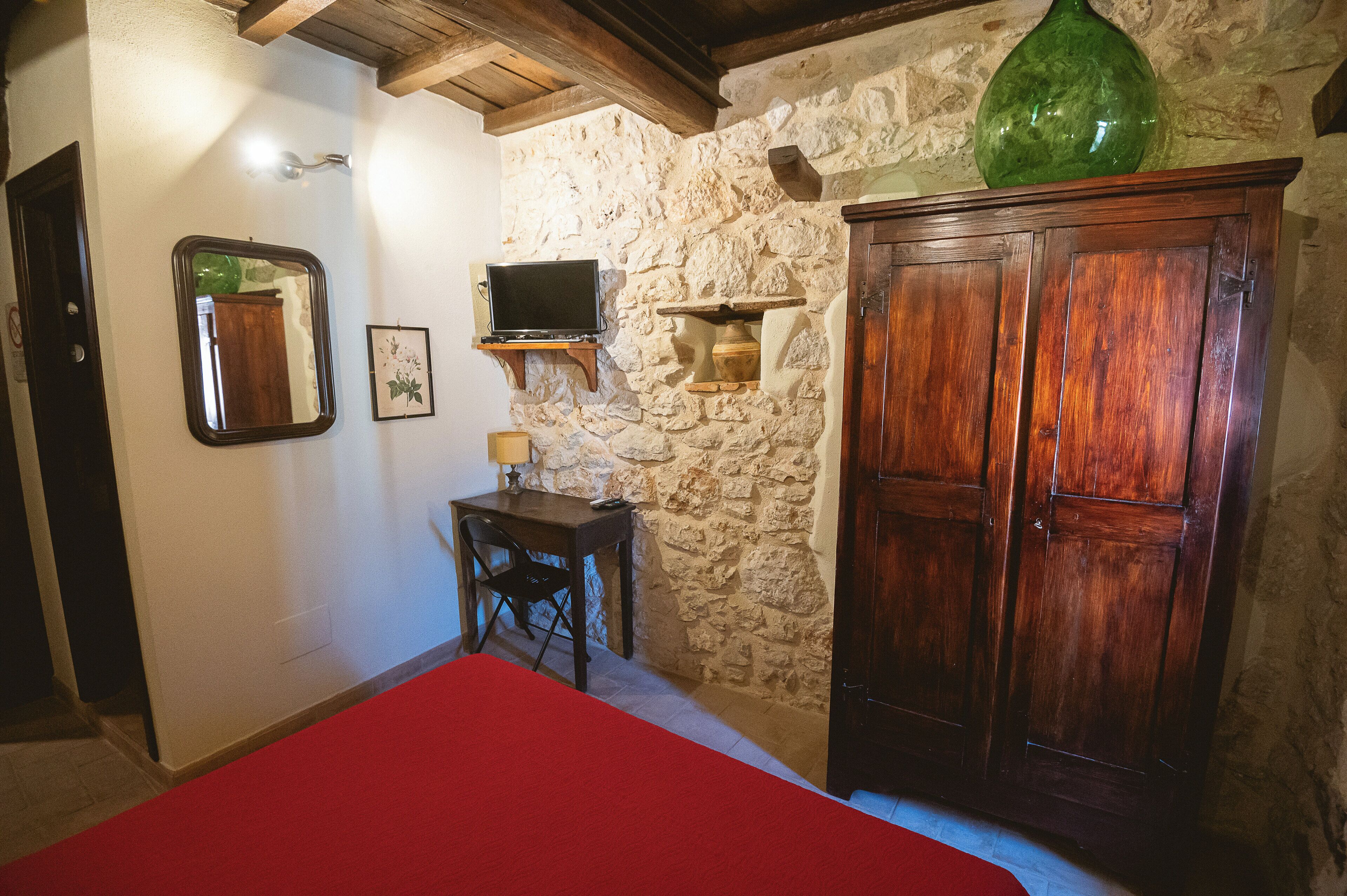 Une pièce avec un mur en pierre, des meubles en bois, une télévision et une couverture de lit rouge.