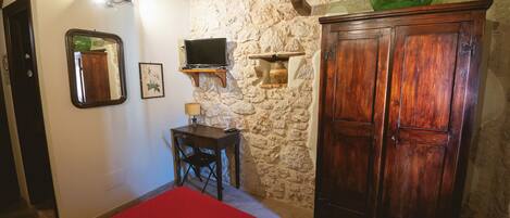 Une pièce avec un mur en pierre, des meubles en bois, une télévision et une couverture de lit rouge.