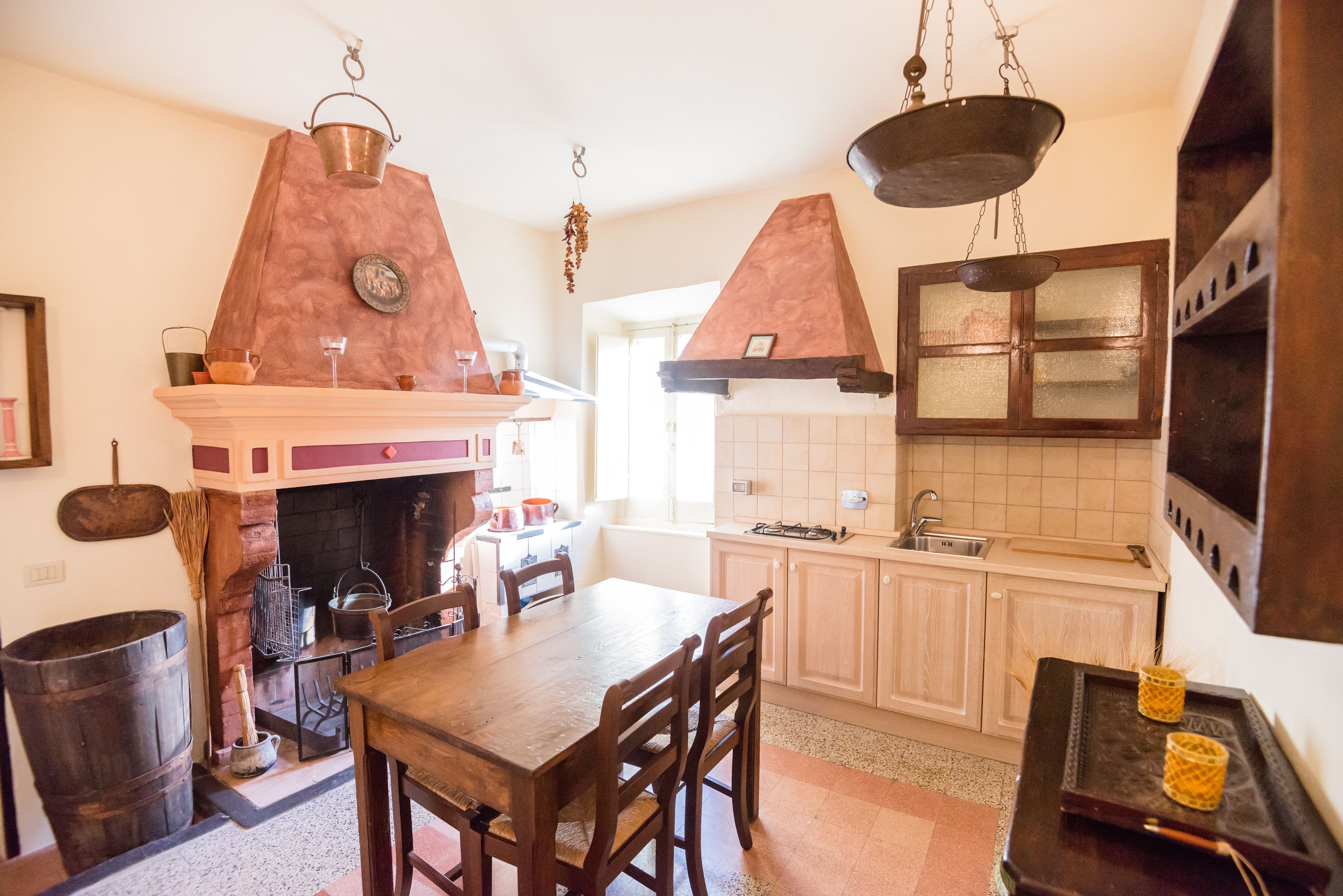 Une cuisine traditionnelle avec une table en bois, des chaises, une cheminée et des casseroles suspendues.